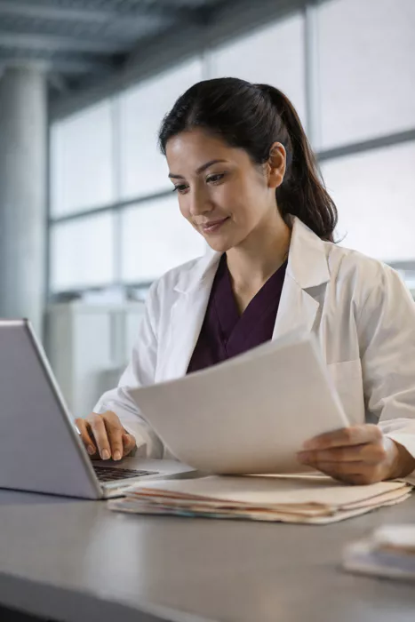 A healthcare professional reviewing clinical paperwork and digital records at a workstation, symbolizing the intersection of medical evidence and AEMPS regulatory compliance.